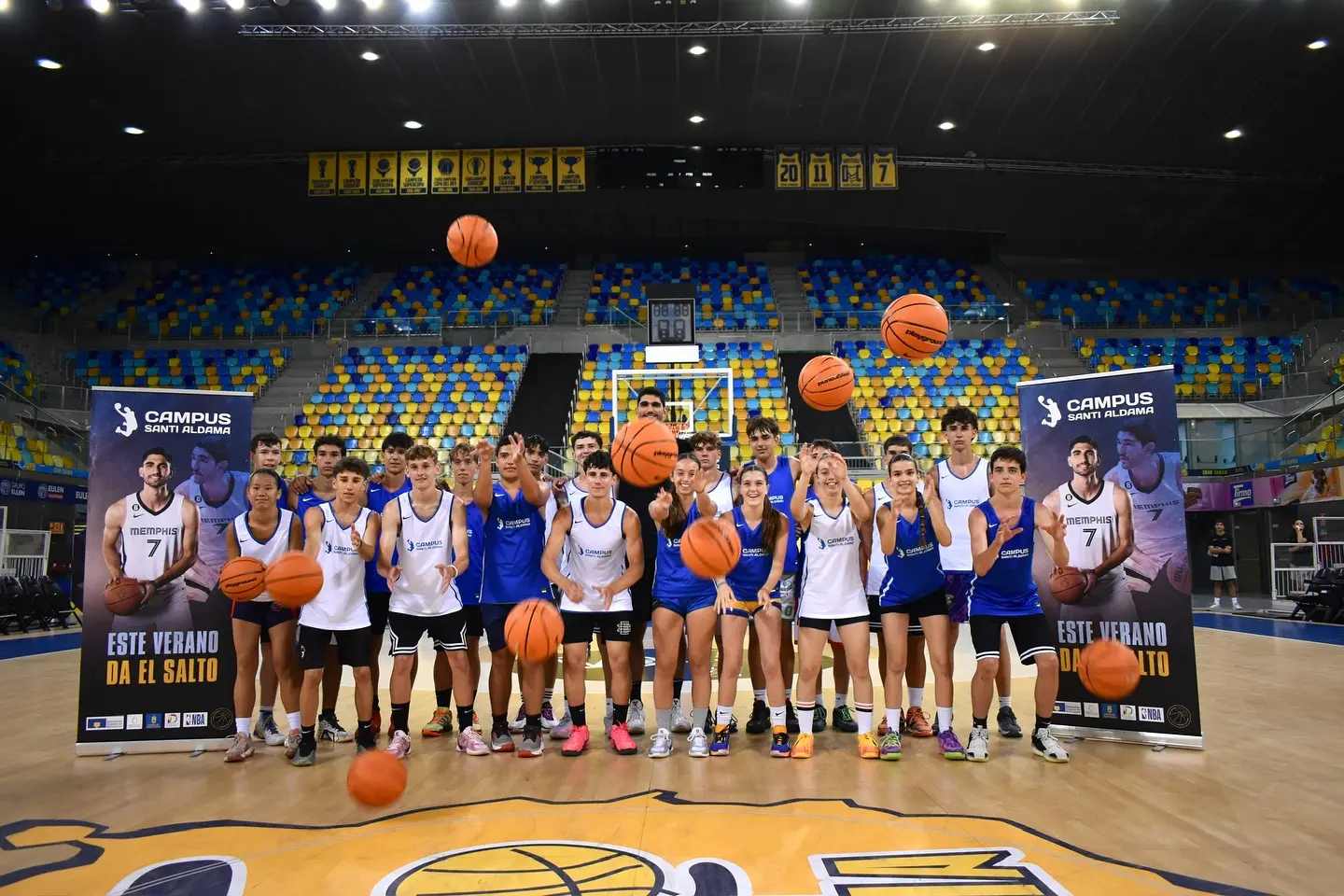 Participantes del Campus Santi Aldama lanzando balones al aire en una foto dinámica sobre el parqué, reflejando el ambiente de diversión y aprendizaje del campamento
