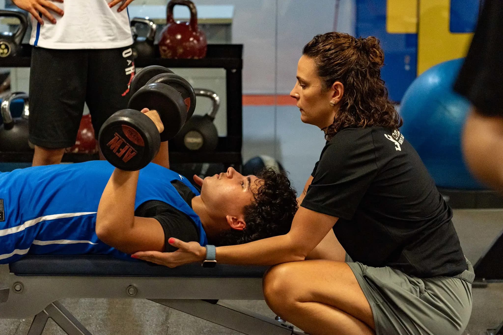 Entrenadora del Campus Santi Aldama supervisando a un alumno en una sesión de preparación física con mancuernas en el gimnasio