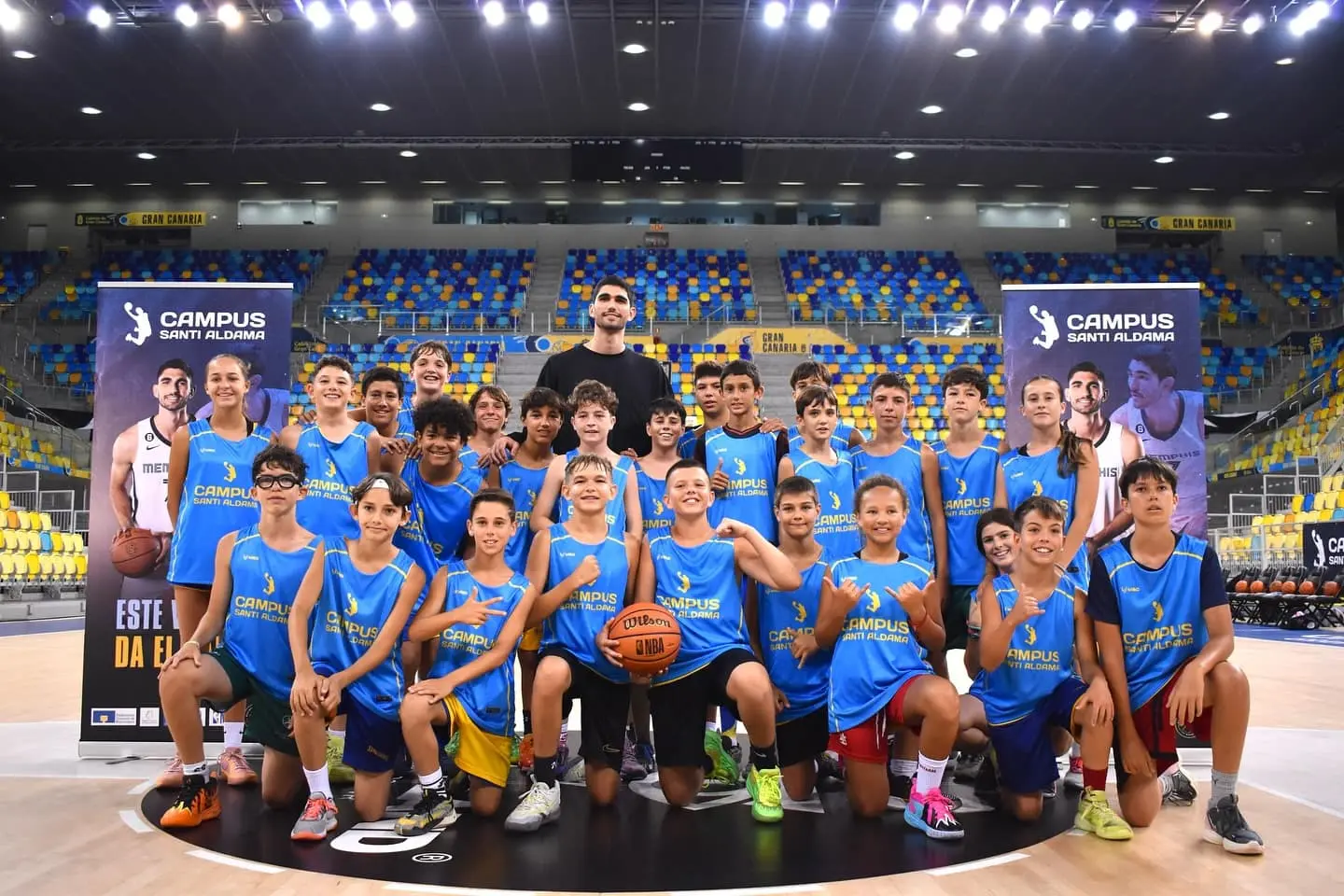 Santi Aldama rodeado de alumnos en el centro de la cancha durante el cierre del Campus Santi Aldama en el Gran Canaria Arena